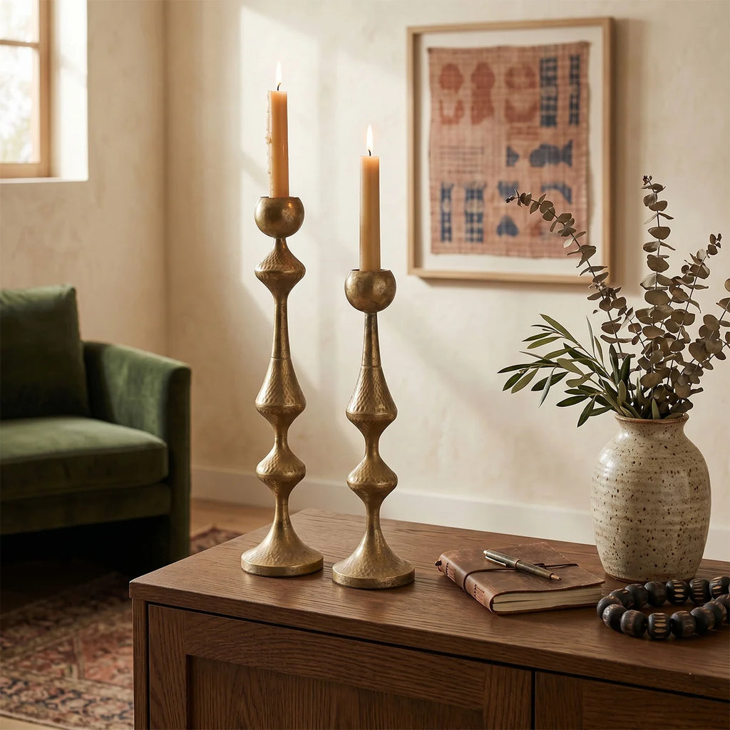 Antique gold candle holders styled on wooden cabinet with vase and notebook