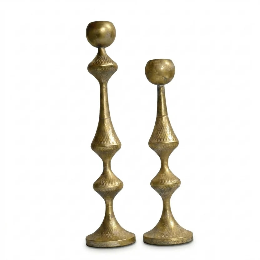 Close-up of two hammered gold metal candle holders against white background