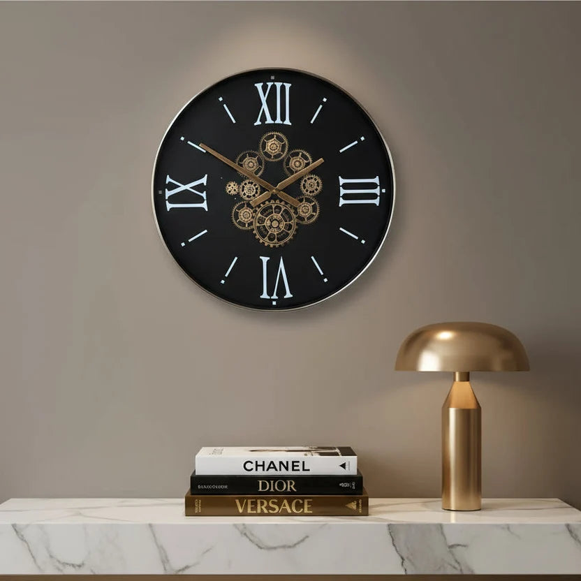Wall clock styled on a beige wall above books and a gold lamp